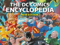 The DC Comics Encyclopedia New Edition hardcover book open on a wooden desk